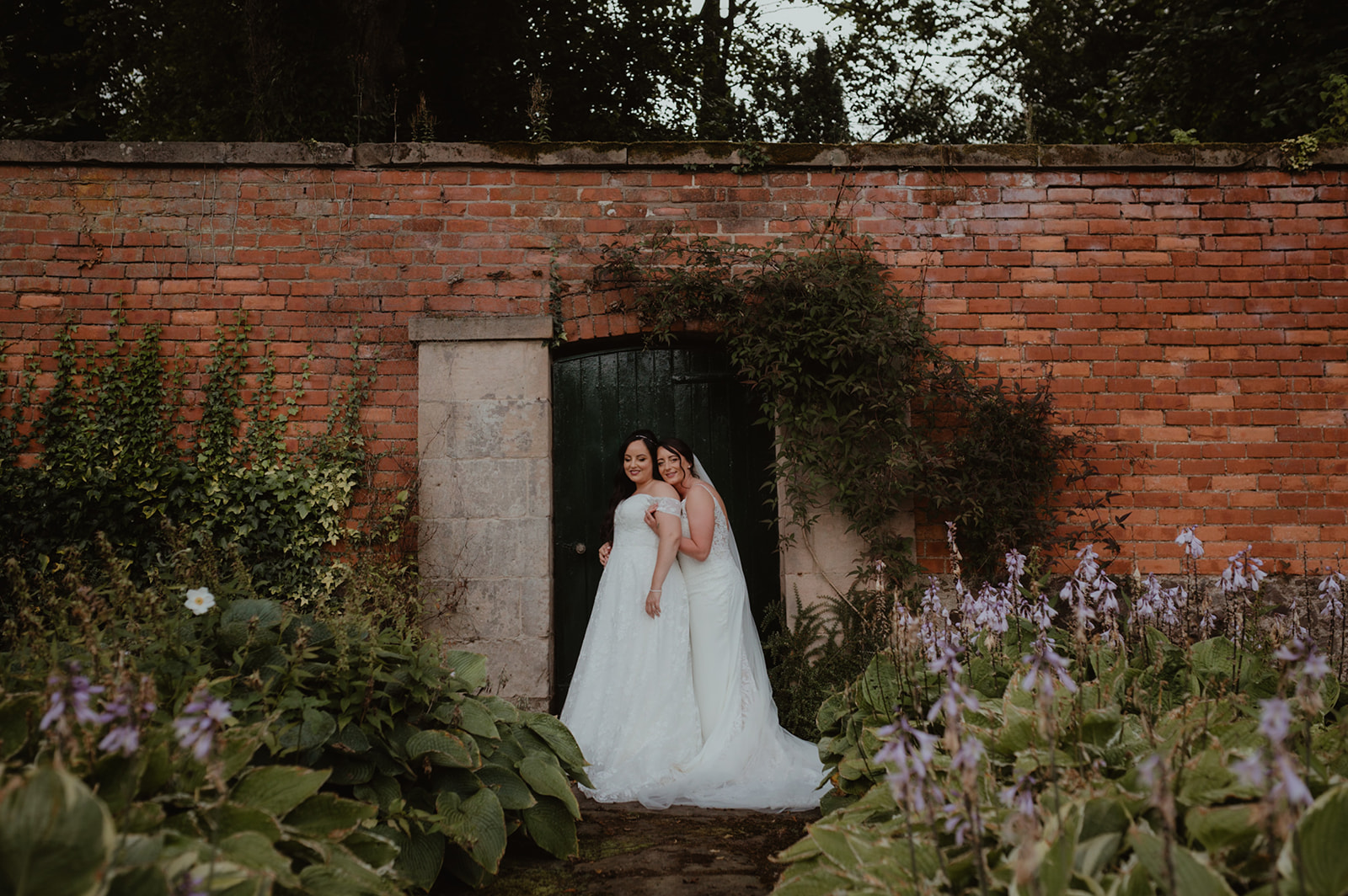 Two brides standing hugging in a walled garden