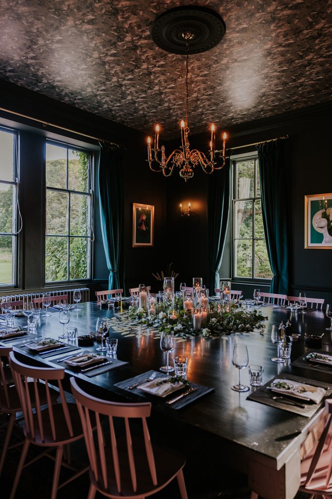 A dark green dining room with a large table decorated with flowers and candles