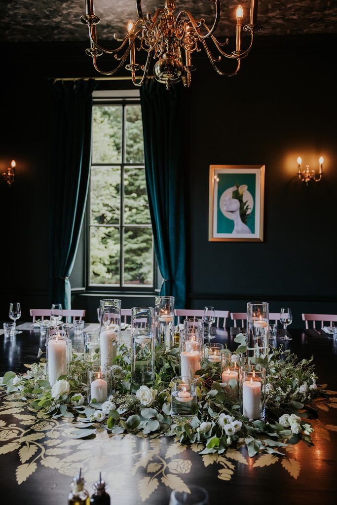 A dark green dining room with a large table decorated with flowers and candles
